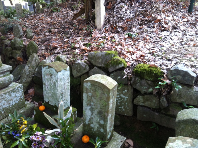 中央の埋め墓を囲う土止めの石積みに古い墓石などが再利用されています。